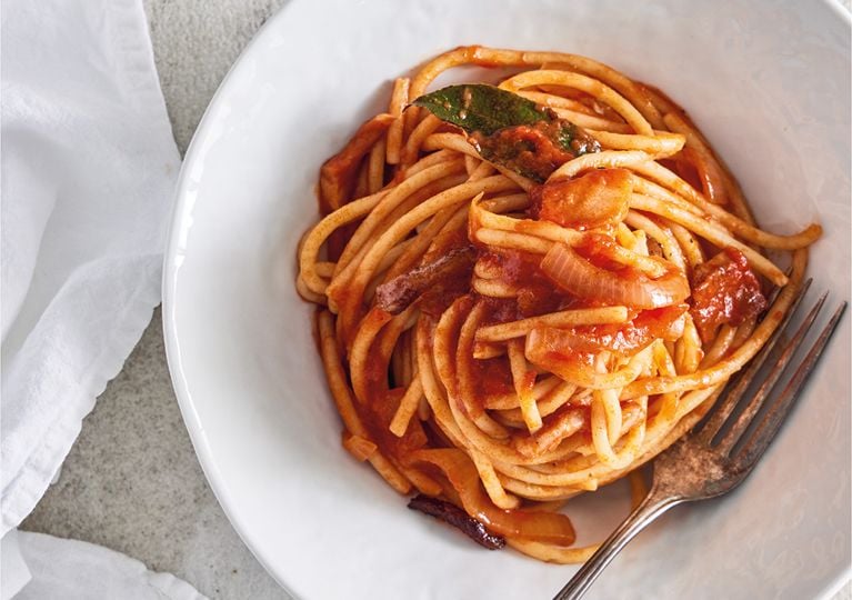 A white bowl filled with bucatini pasta in a tomato sauce.