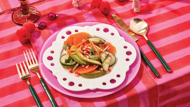 A white plate of jicama and orange salad on a pink and red striped tablecloth.