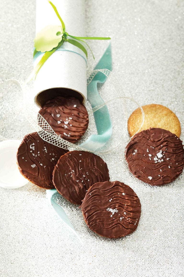 Chocolate-Walnut Thins made with ground oats and nuts covered with thin chocolate spilling from a gift cookie tube adorned with blue and green ribbon for a post on a delicious Chocolate-Walnut Thins recipe