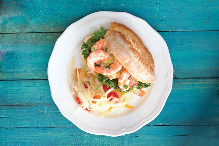 An easy shrimp sandwich, featuring cooked shrimp mixed with mayonnaise, sweet pickles, green onion, and paprika, piled high on a toasted Italian bun lined with leafy lettuce.
