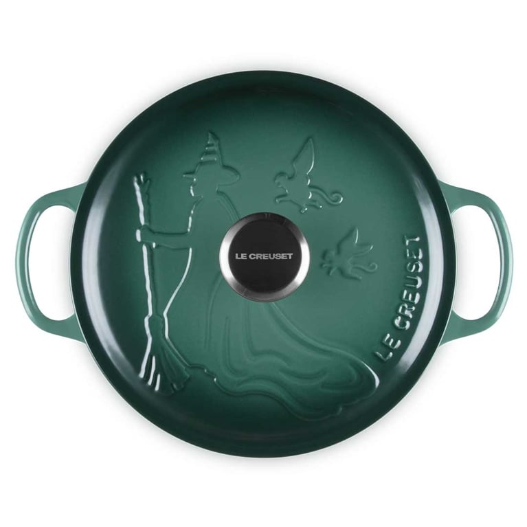 An artichaut green Le Creuset dutch oven lid shown from above with an embossing of Elphaba from wicked and two flying monkeys