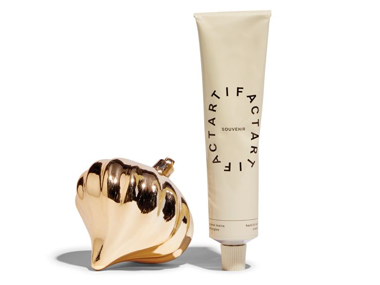A tube of Artificate hand and nail cream next to a gold Christmas ornament