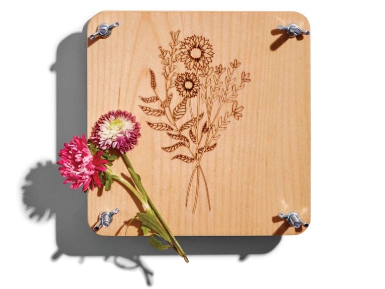 A wooden flower press from brand LivCan with a wildflower sitting atop it.