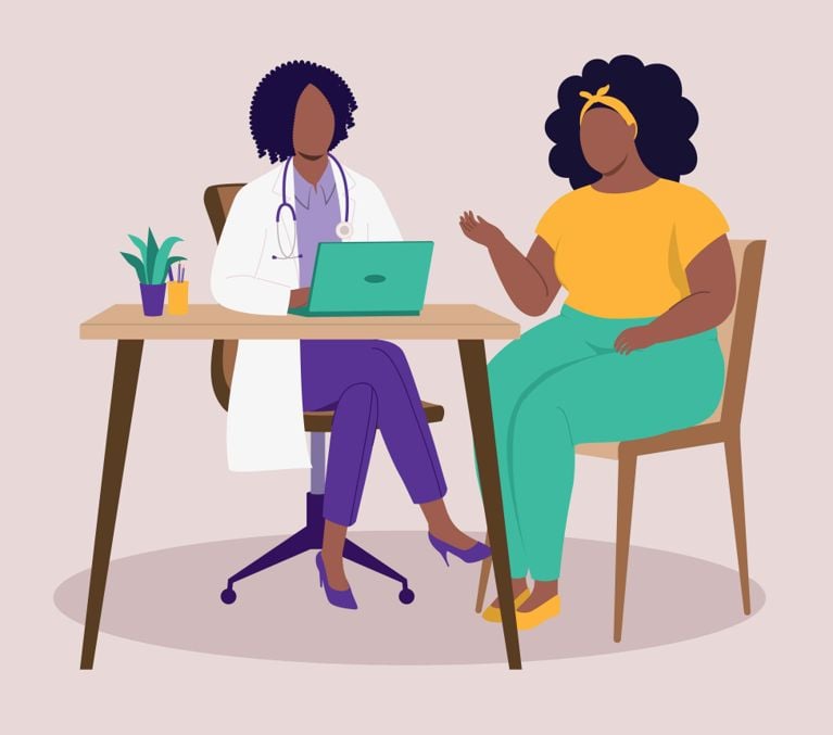 a doctor in a white lab coat with a stethoscope and a lap top sits at a desk and speaks to her patient, who is also sitting on a chair facing her, for a piece on the Addressing The Menopause Gap For Black Women