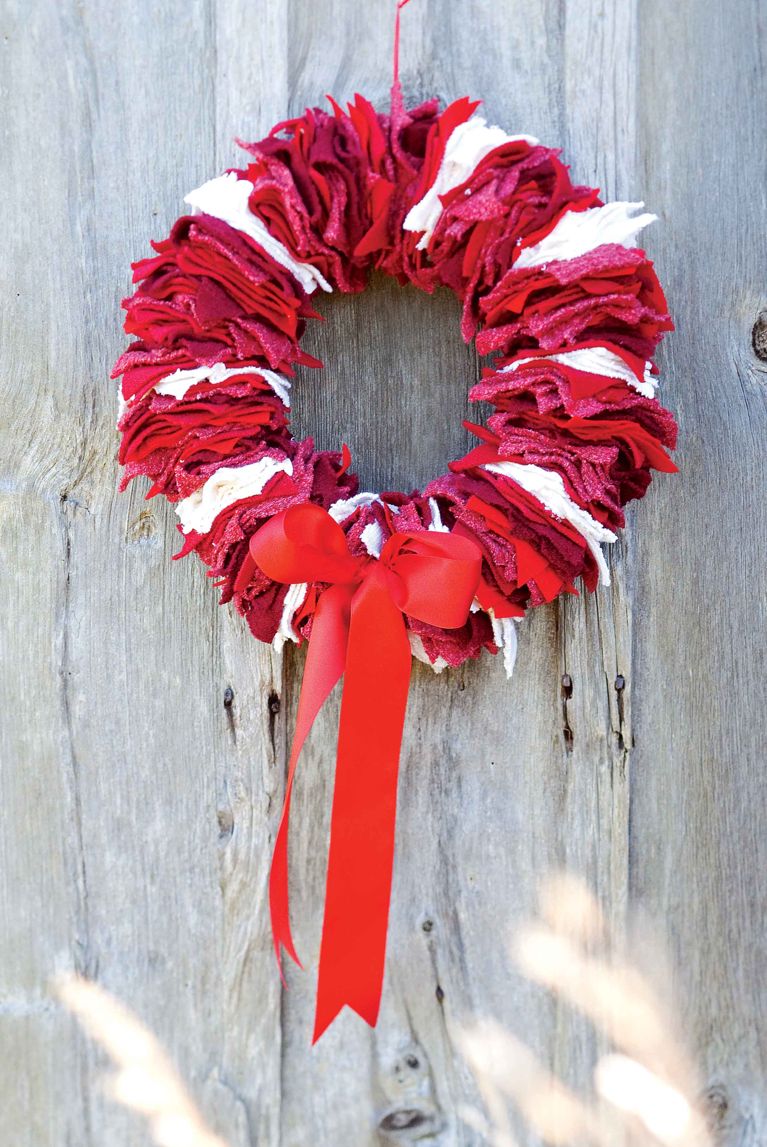 a homemade wreath made of old sweater scraps in red and white with a red ribbon