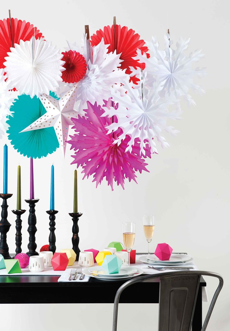 An array of paper snowflakes hanging over a table decorated for the holidays with stems of champagne and colourful cubes