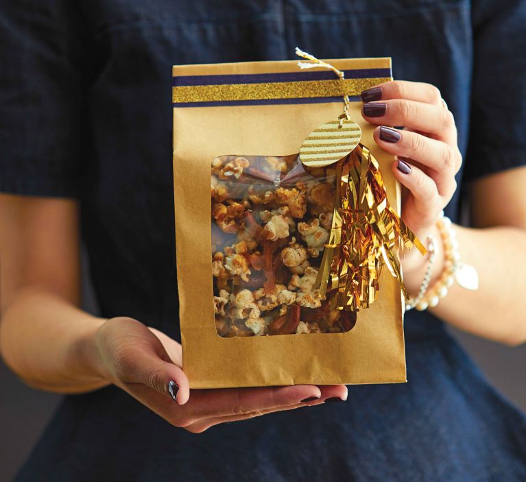 a bag of homemade salted caramel popcorn with two hands holding it presented as a gift