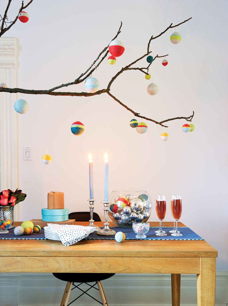 a set of homemade yarn-wrapped colourful christmas ornaments hanging from a tree branch over a festive table
