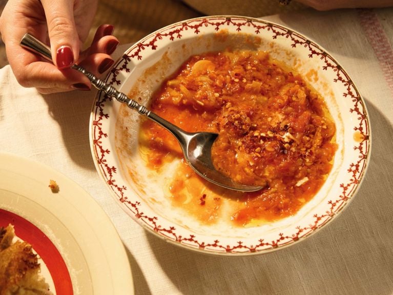 A bowl of Alison Roman's rich buttered tomato soup with lentils and fennel, topped with a dollop of sour cream and red pepper flakes.