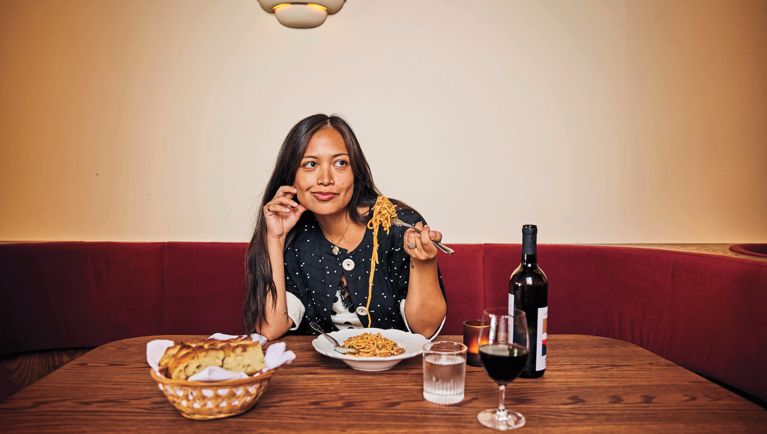 Marlowe Granados sits alone in a banquette booth enjoying a bowl of pasta and a glass of red wine.