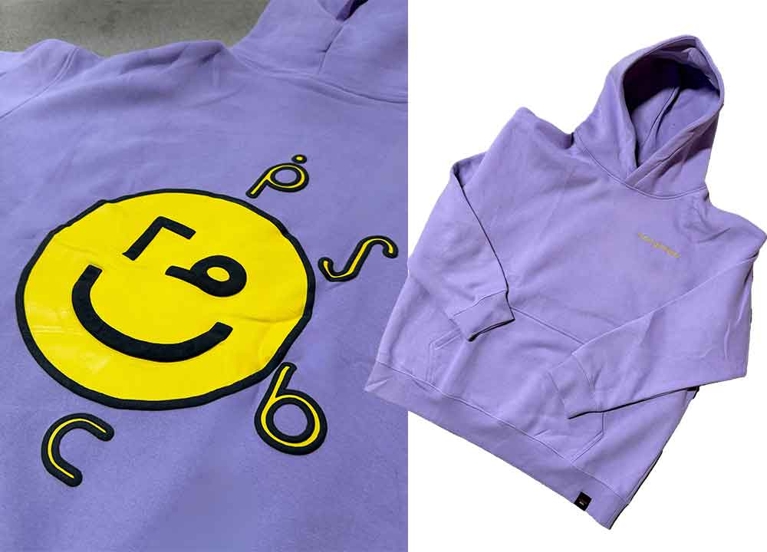 A purple Aaniin hoodie with a yellow smiley face that reads “Mino Giizhigad”—or “it’s a good day.”
