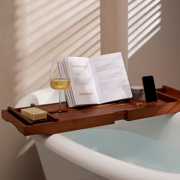 A Simons Home bath caddy seen on a bathtub with a book on it for an article about the best self-care gifts for pampering for the holidays.