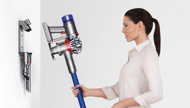 A photo of a woman putting a Dyson into its wall mounted dock in a post about best stick vacuums dog.