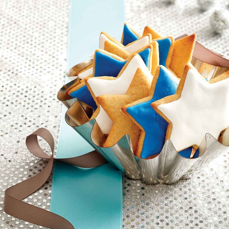 A bunch of start-shaped cookies with blue and white frosting in a silver dish.