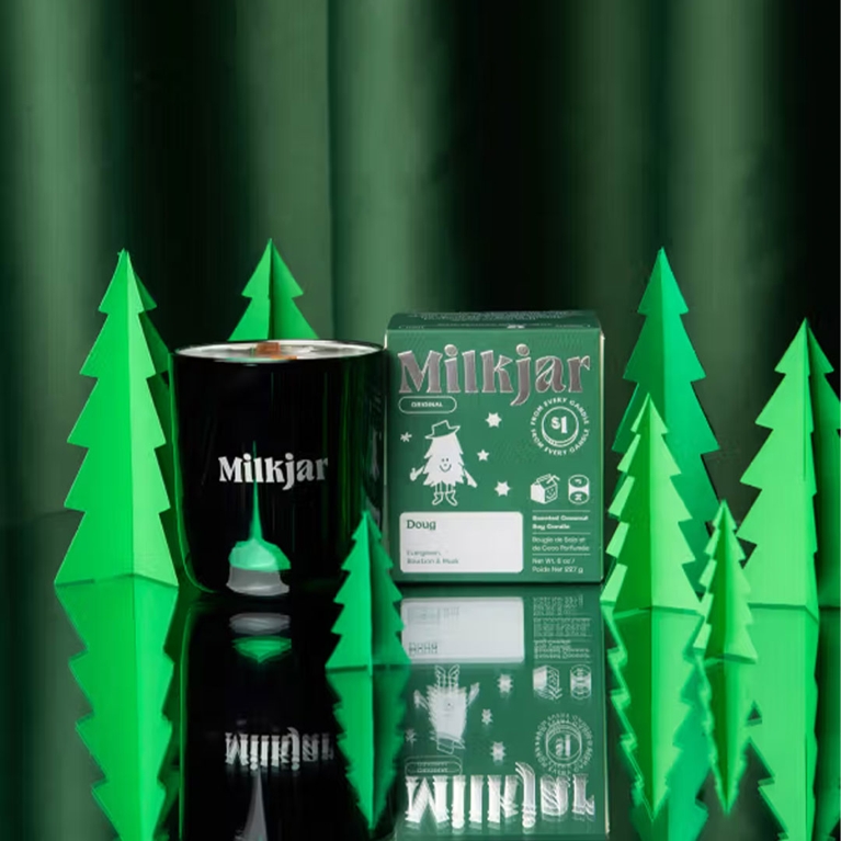 A metallic green candle next to its green box and some green trees on a metallic background for a post on gifts that give back.