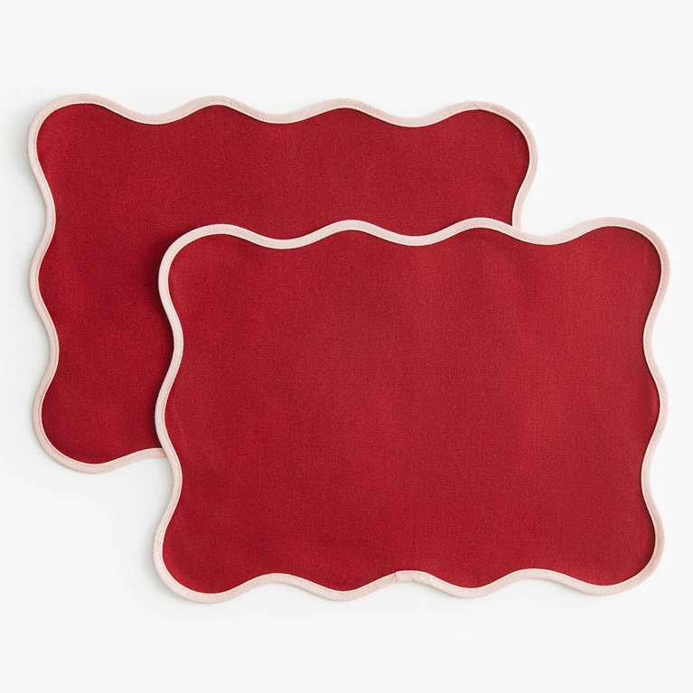 Two red and pink scalloped placemats for an article about the best H&M Home holiday decor pieces for 2025.
