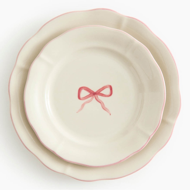 A white plate with a pink border and a pink brow in its centre for an article about the best H&M Home holiday decor pieces for 2025.