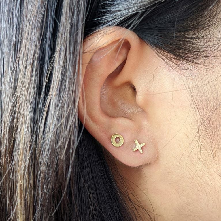 a pair of brass marmalade designs sculpted stud earrings in x o worn on one ear