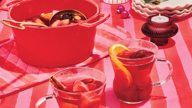 Two glasses of red hibiscus Christmas punch next to a red pot and ladle, in a post about a Feliz Navidad menu.