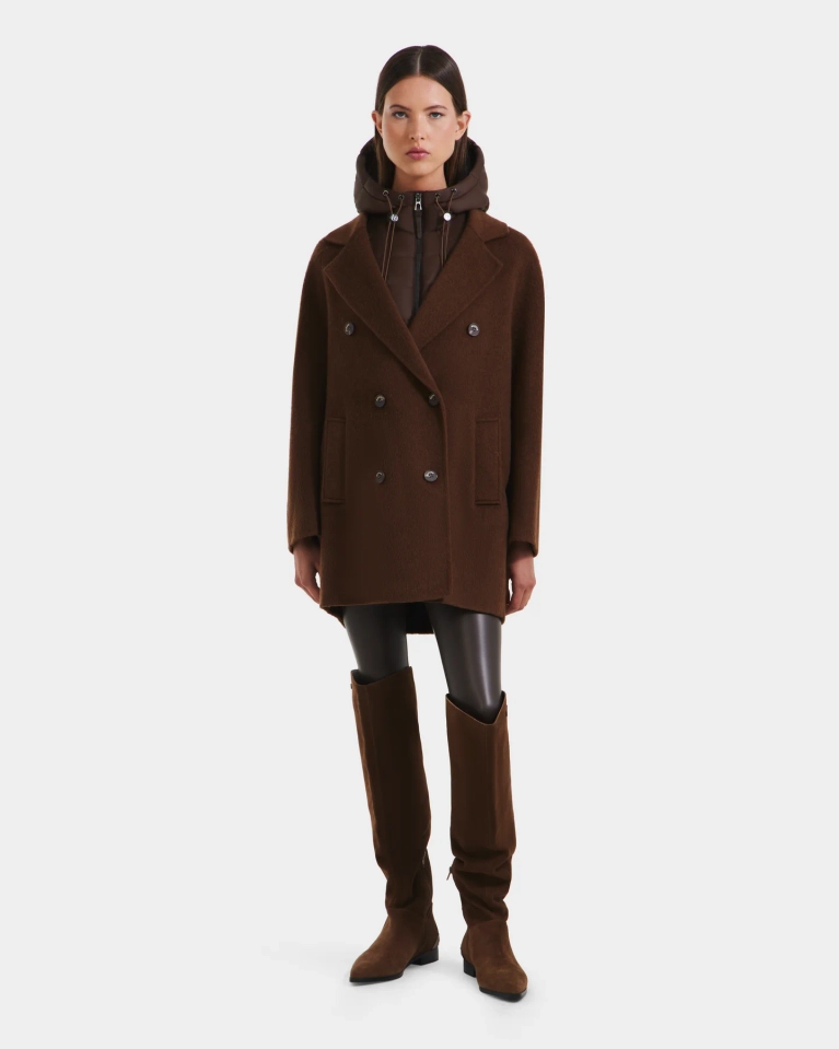 A full-length studio photograph of a woman wearing the Rudsak Bethany wool coat in brown, layered over a darker brown hooded jacket. The double-breasted coat is short in length. She is also wearing dark leggings or leather pants and a pair of tall, brown suede boots, positioned against a white background. This image is associated with a Black Friday promotion.