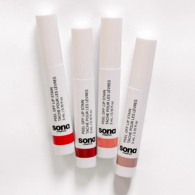 Four tubes of Sona Cosmetics Peel Off Lip Stain, with white caps and bases dipped in different shades of red, pink, and nude. The tubes are arranged diagonally on a white background.