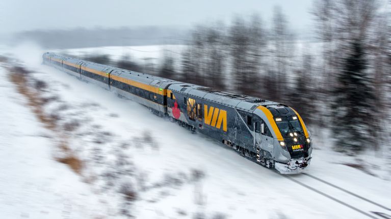 A bird's-eye view of a VIA Rail train driving through Quebec in the snow, in a post about the VIA Rail Canada Strong pass for holiday travel.