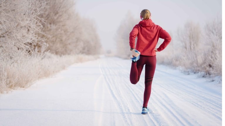 A woman stretching in running gear on a wintry road in a post about apple fitness workout buddy.