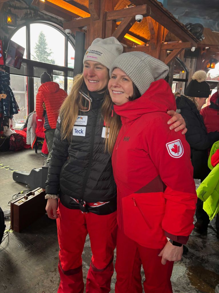 Canadian alpine skier Valérie Grenier (left) and a companion named Gillian pose together smiling in a ski lodge. Grenier wears a black sponsor jacket and red pants, while Gillian wears a red Team Canada jacket.