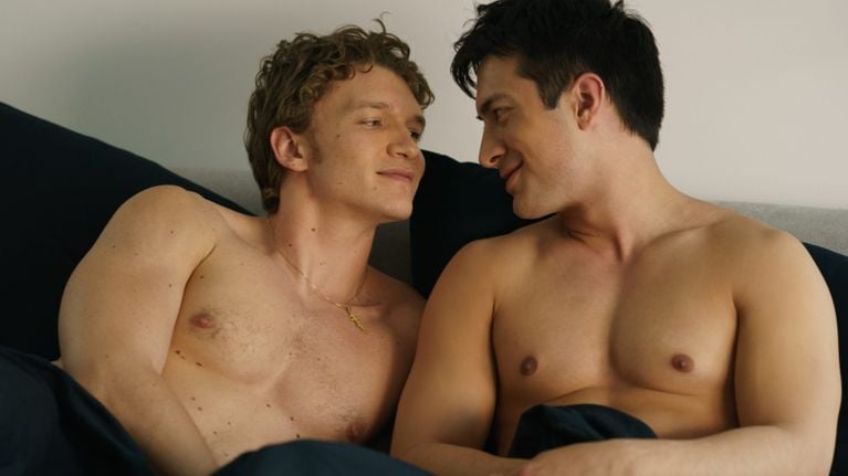 Two young men—Connor Storrie as Ilya Rozanov and Hudson Williams as Shane Hollander—smile at each other in an intimate bedroom scene.