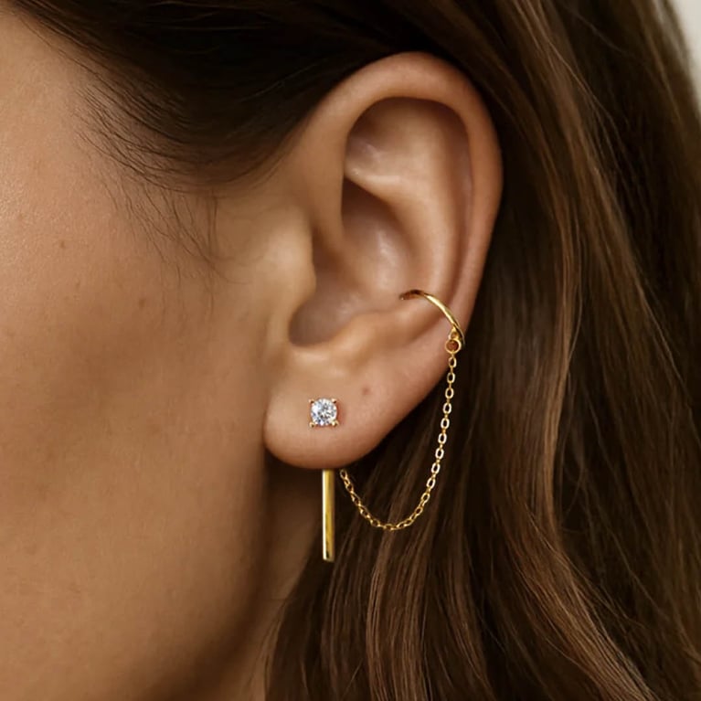 Image of an ear wearing an earring attached to an ear cuff by a gold chain.
