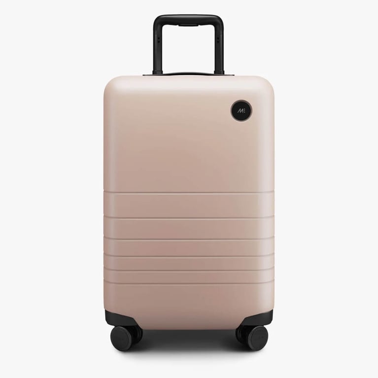 A photo of a pink hard shell carry-on suitcase with wheels.