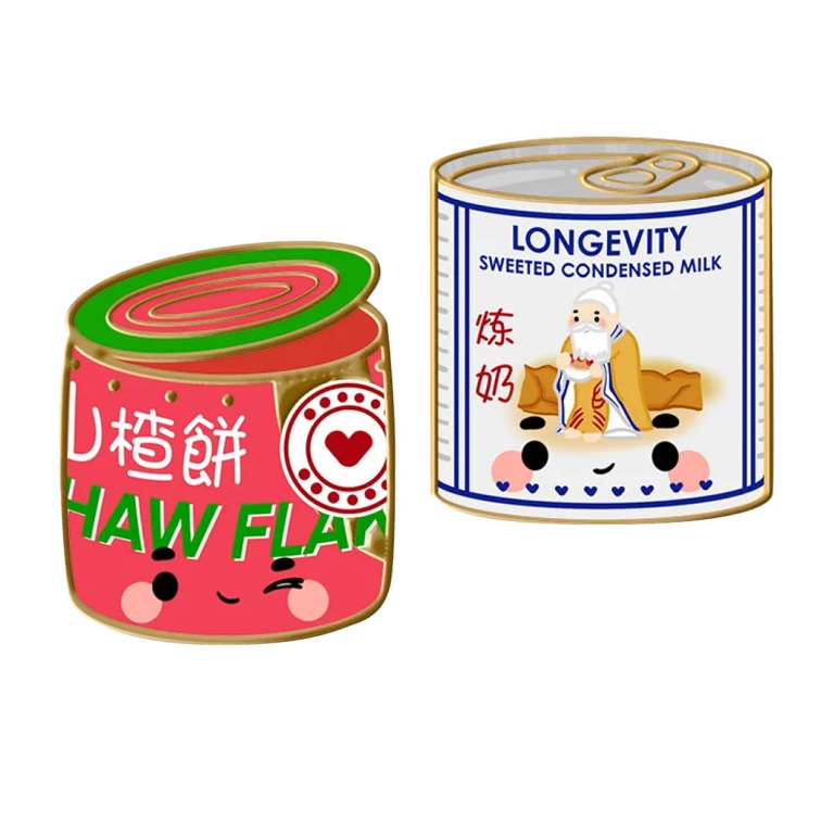 Photo of two enamel pins, on the left is a roll of Haw Flakes, on the right is a can of sweetened condensed milk. 