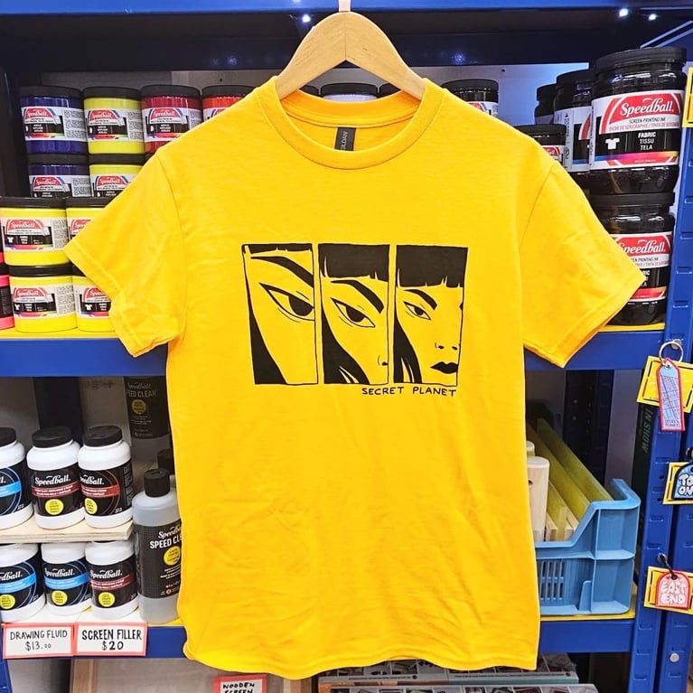 Photo of a yellow tshirt with a illustration of a face.