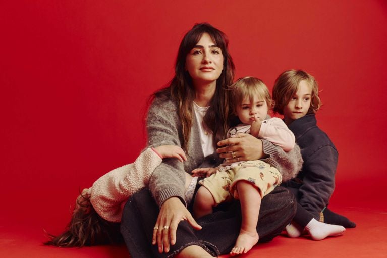 Author Amil Niazi sits on a red backdrop with her three children on her lap.
