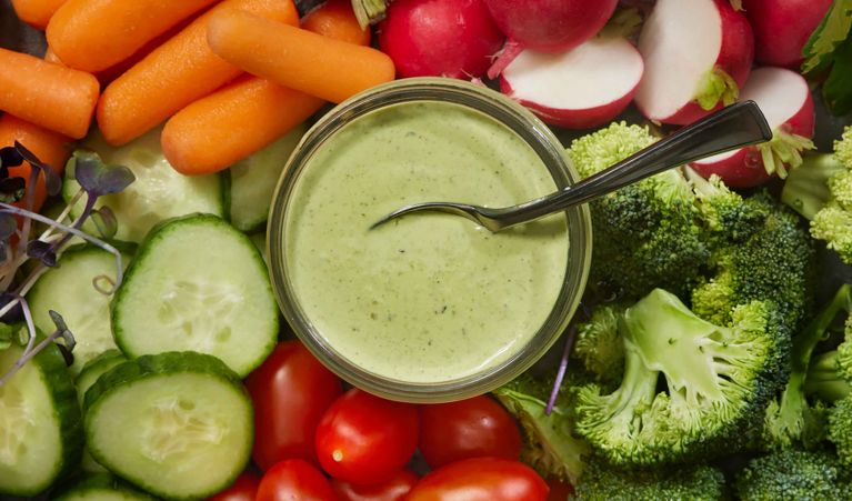 A bowl of Green Goddess dip served with a variety of fresh dipping vegetables like carrots, tomatoes, and broccoli.