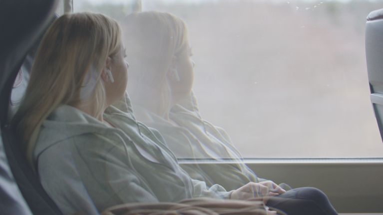 A blonde woman, Jessica Baker, looks out the window of a train.