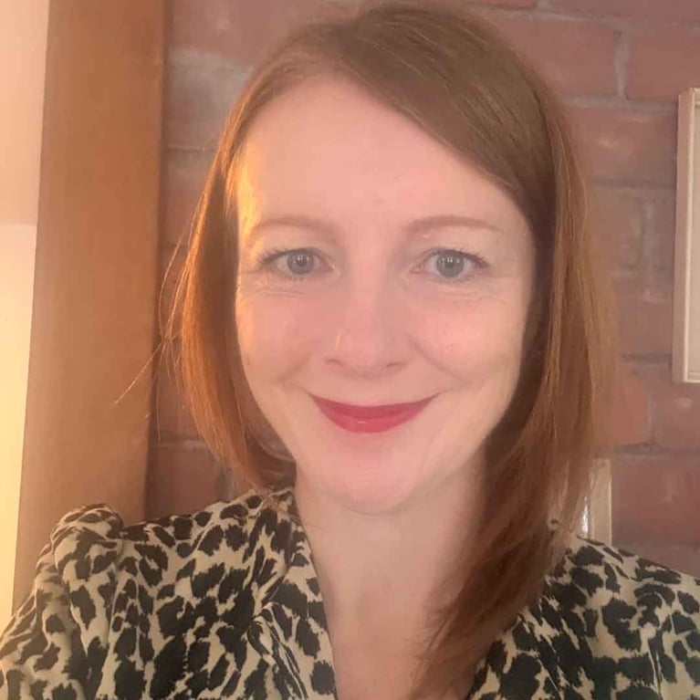 A photo of a woman with red hair and a leopard bolero standing against an exposed brick wall, in a post about midlife beauty.