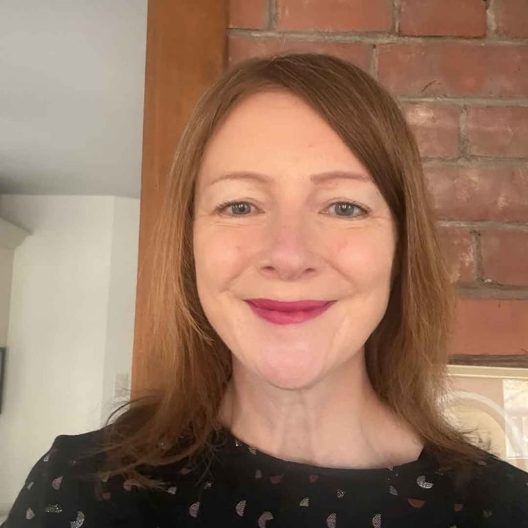 A photo of a woman with red hair and a black shirt standing against an exposed brick wall, in a post about midlife beauty.