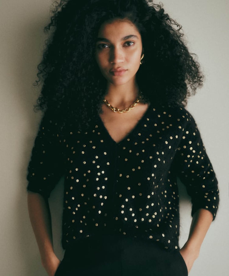 A model wearing a black cardigan with gold polka dots from Sézane to illustrate the polka dot trend.