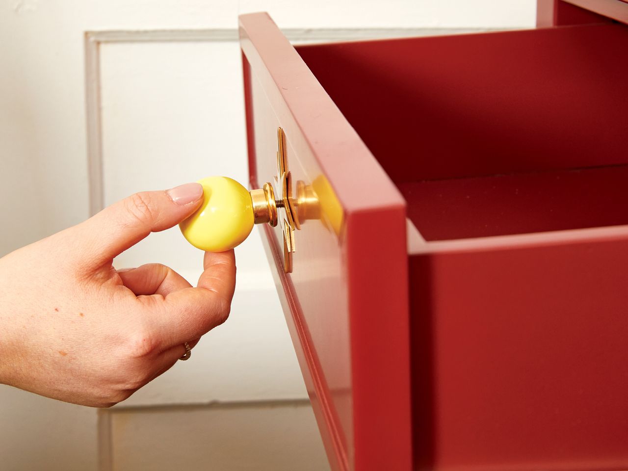 Decor expert Alexandra Gater installing new yellow hardware on a burgundy nightstand for an article about easy DIY home decor projects.