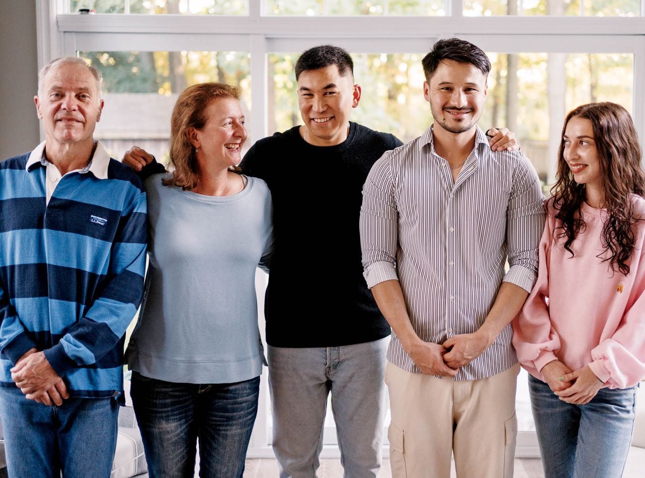 A family stands in a line, smiling. The Long family (Doug, Wendy and daughter Véronique) has sponsored five young men, including Ibrahim and Ali.