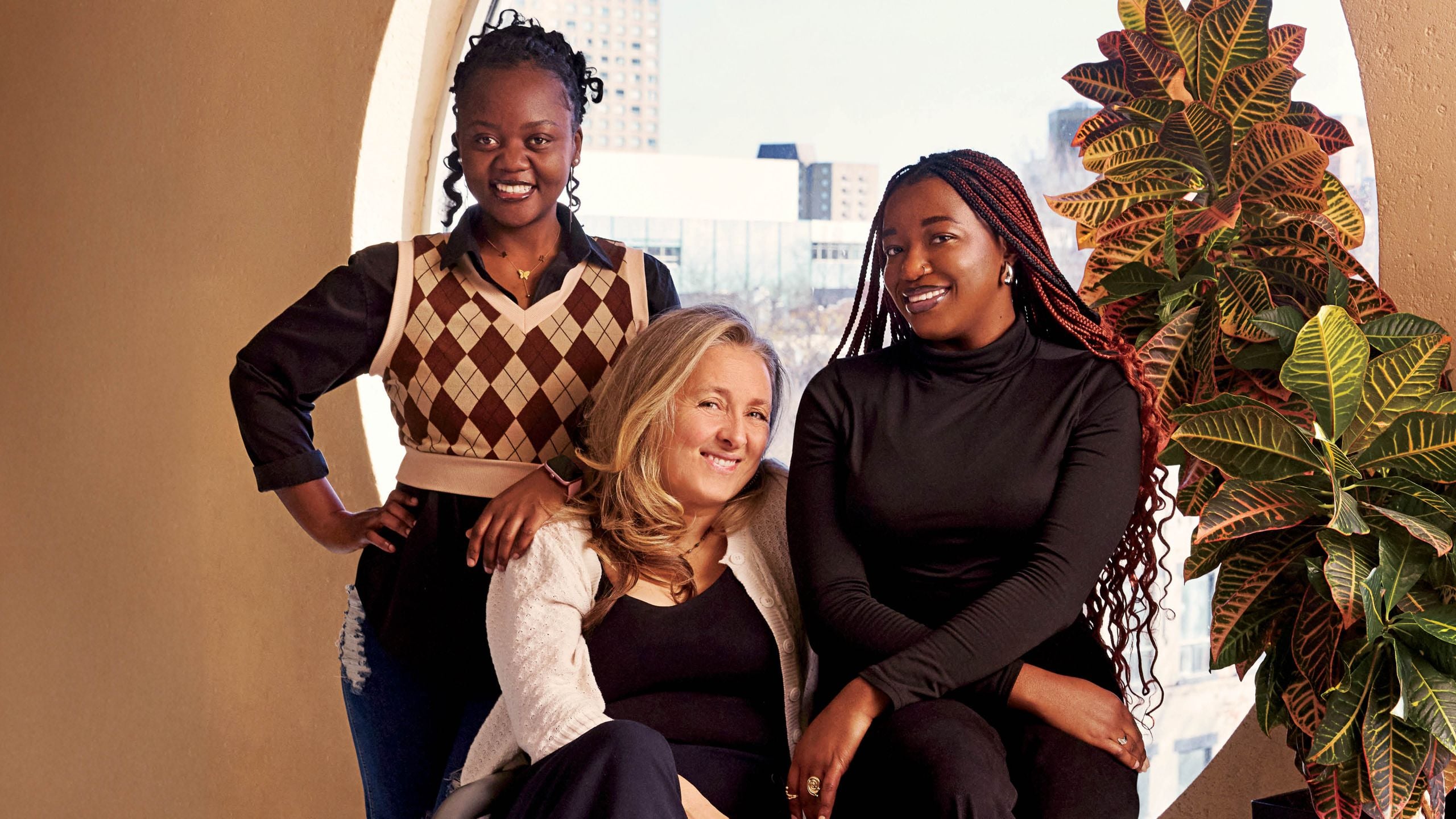Three women sit in front of a window, smiling. Rafaëlle Sinave, centre, became a maternal figure to Valentine Uwimanale, left, and Merveille Mufala after she sponsored them.