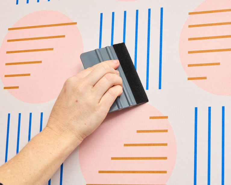 A woman smooths the air bubbles while installing peel-and-stick wallpaper.