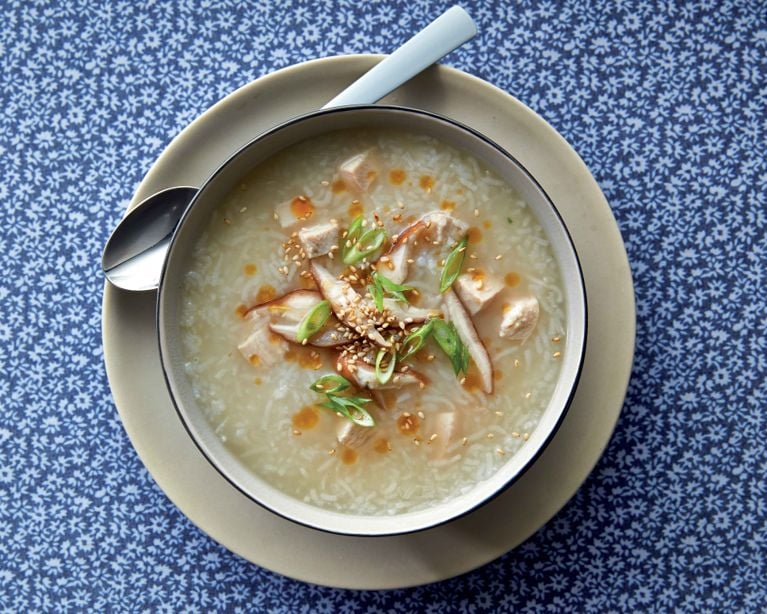 Savoury chicken congee recipe topped with ginger, sesame seeds, and green onions. Healthy Asian rice porridge breakfast bowl with shiitake mushrooms and chili oil garnish.