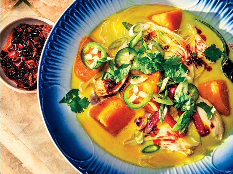 A blue bowl filled with golden Coconut Broth with Noodles, Sweet Potato and Leftover Protein.