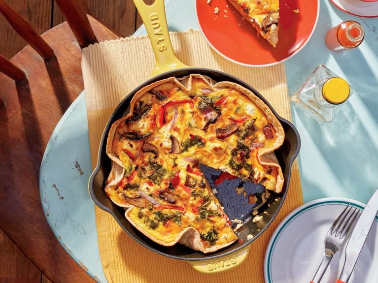 A yellow skillet filled with Mushroom, Pepper, Kale And Goat Cheese Quiche.