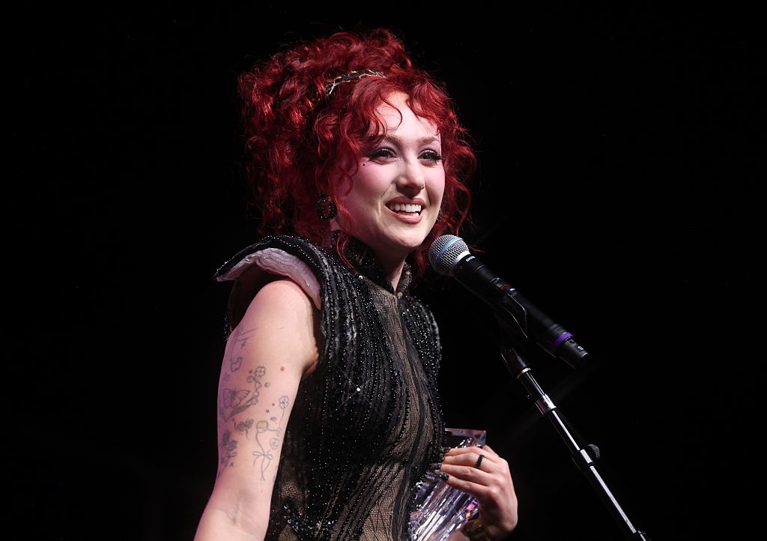 A photo of a woman with curly red hair at a microphone in a post about chappell roan apology.