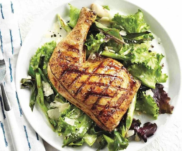A chicken thigh served on top of a mixed green salad on a white plate