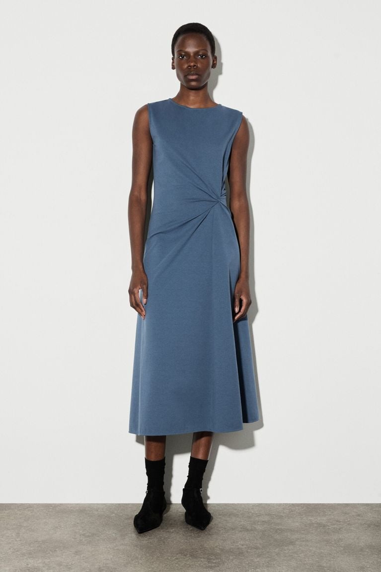 A woman standing in a blue midi dress for a post on COS Canada online.
