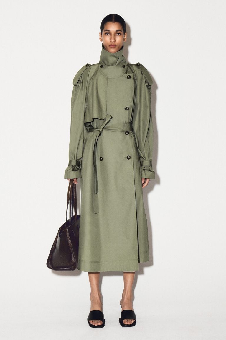 A woman standing in a trench coat for a post on COS Canada online.